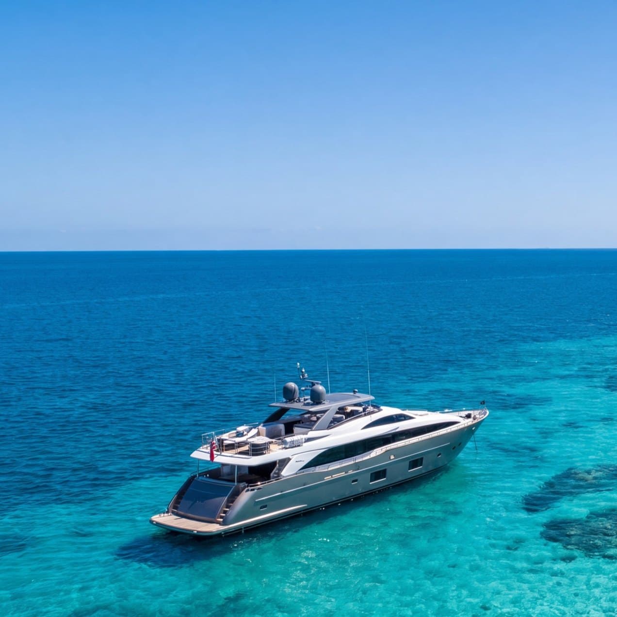 A motor yacht anchored in clear turquoise water off a sunlit beach