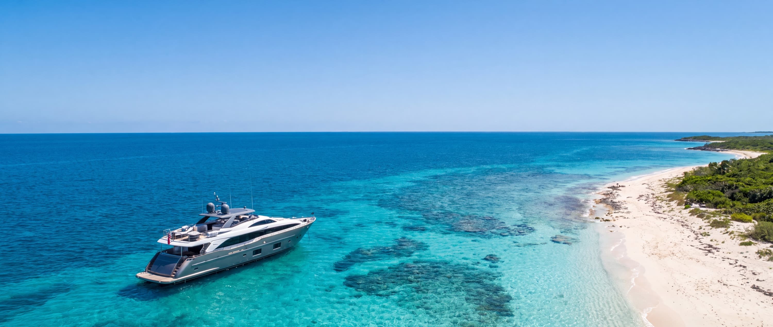 A motor yacht anchored in clear turquoise water off a sunlit beach
